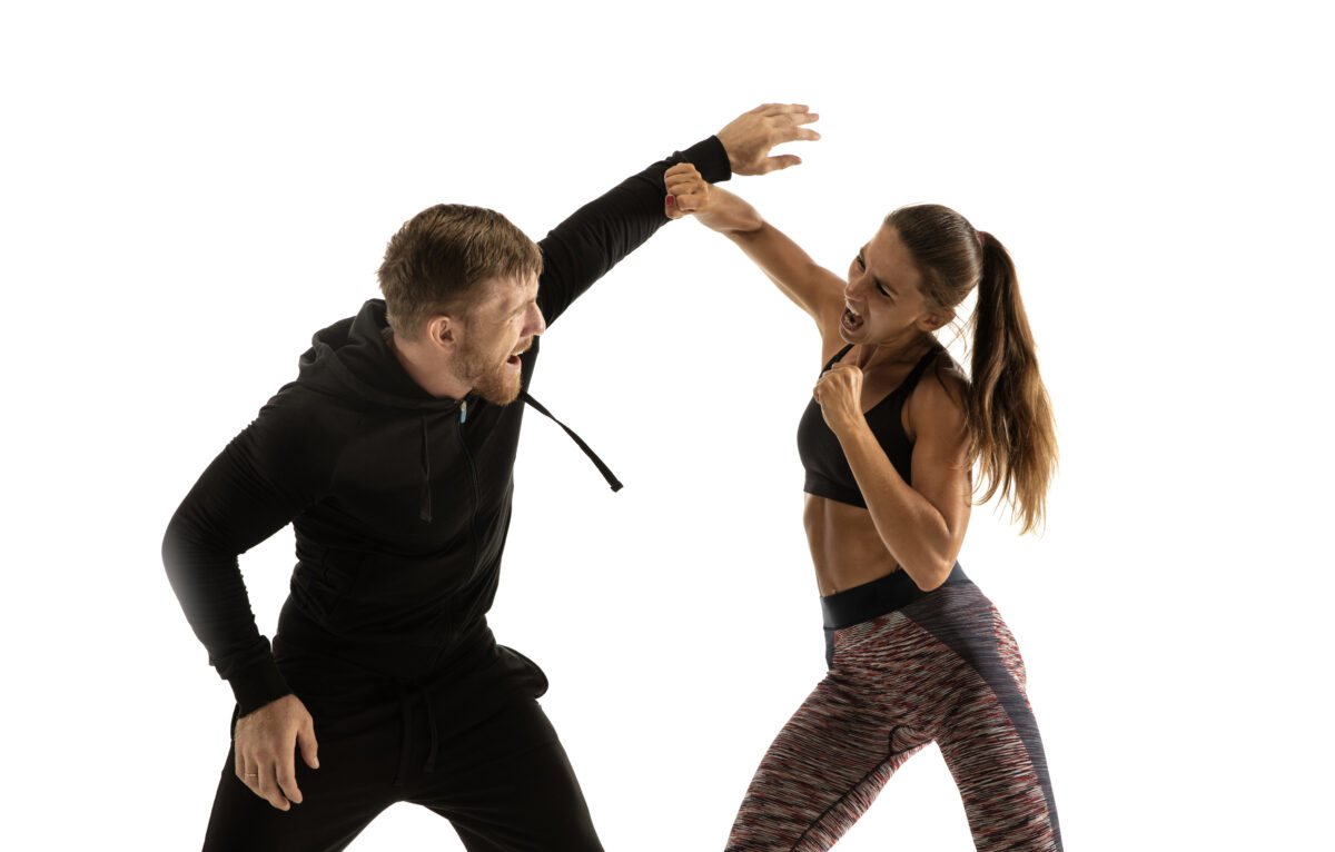 Man in black outfit and athletic caucasian woman fighting on white studio background. Women's self-defense, rights, equality concept. Confronting domestic violence or robbery on the street. ©