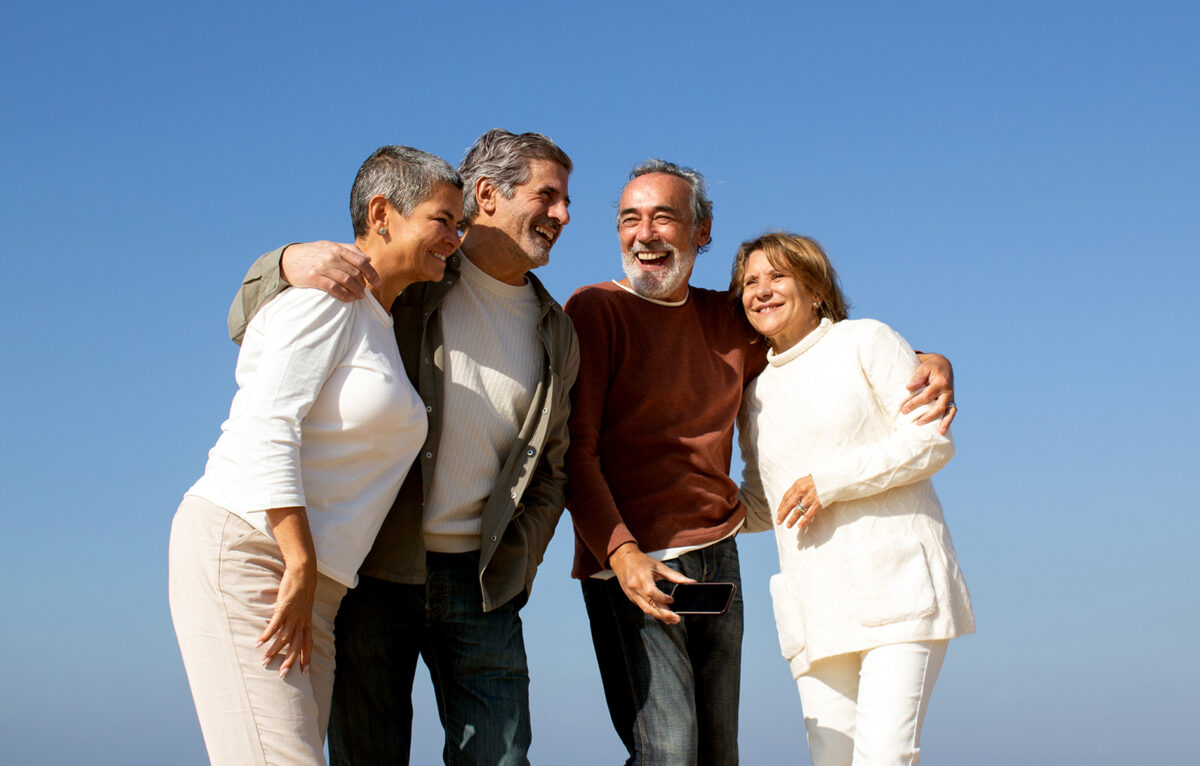 Two senior couples having fun outdoors on sunny day, standing against blue sky and laughing. Happy old friends enjoying leisure time together. Friendship, leisure, retirement concept ©